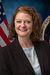 Tina Bayuse smiling in a formal portrait with a U.S. flag behind her.