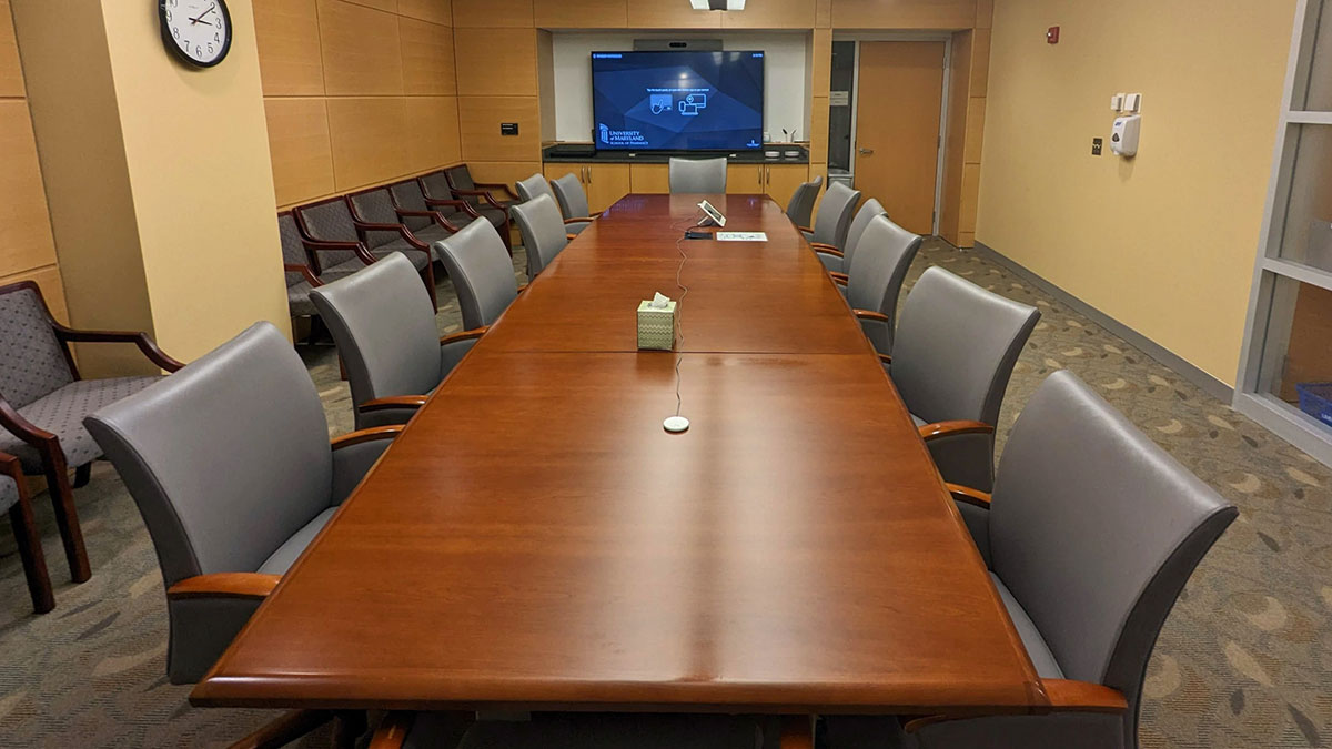 Dean’s conference room in Pharmacy Hall North with a long conference table surrounded by chairs, a wall‑mounted display at the front, and additional seating along the wall.