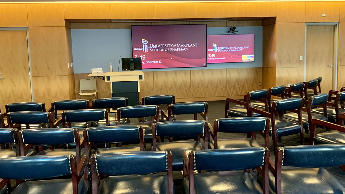 Lecture and presentation room HSF 2‑600 with rows of audience chairs facing a lectern and two large wall‑mounted display screens.