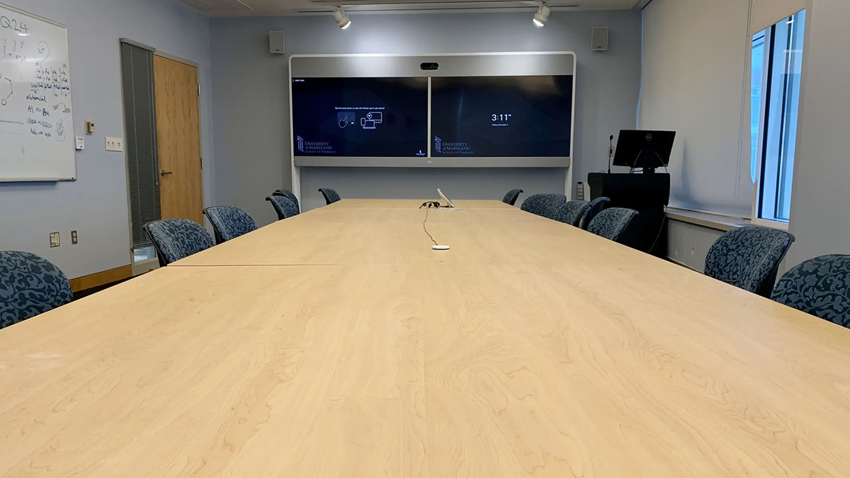 Conference room HSF 2‑541 with a long meeting table surrounded by chairs, dual wall‑mounted display screens, whiteboard, and video‑conferencing equipment.