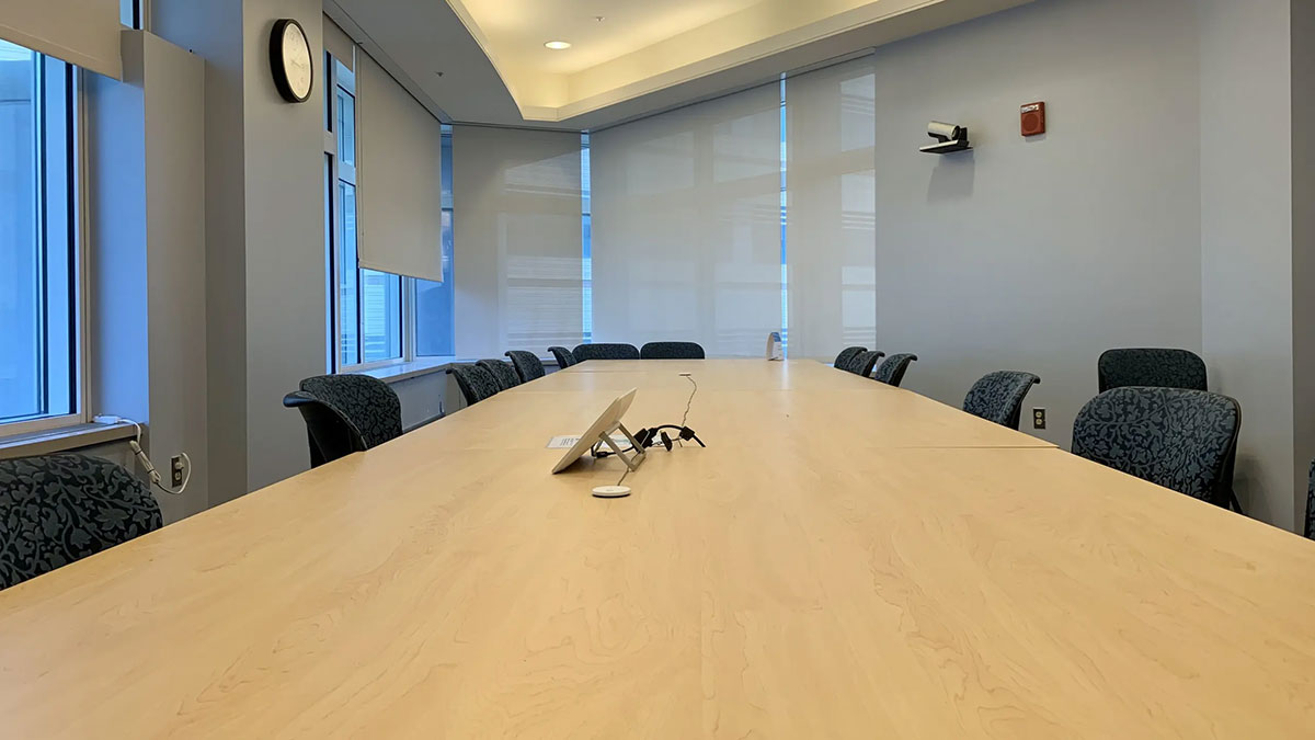 Alternate angle of conference room HSF 2‑541 with a long meeting table, rolling chairs, tabletop control panel, and windows along one wall.