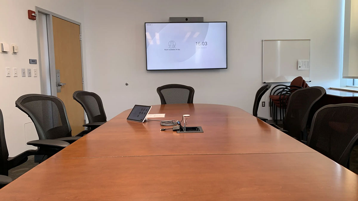 Conference room in Pharmacy Hall North with a rectangular meeting table, rolling chairs, and a wall‑mounted display screen at the front.