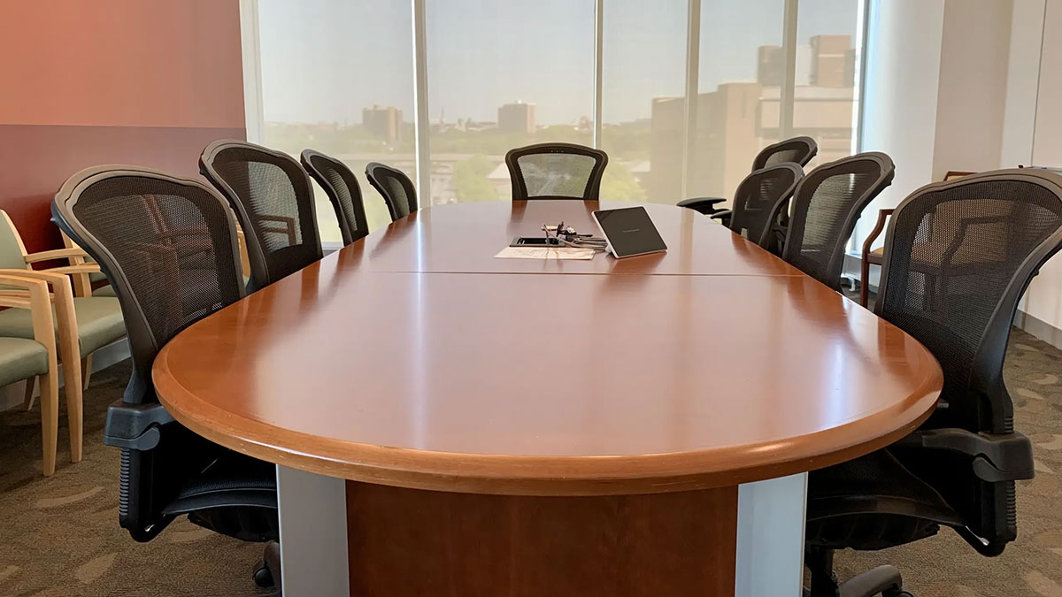 Alternate view of a Pharmacy Hall North conference room with an oval meeting table, rolling chairs, and large windows along one wall.