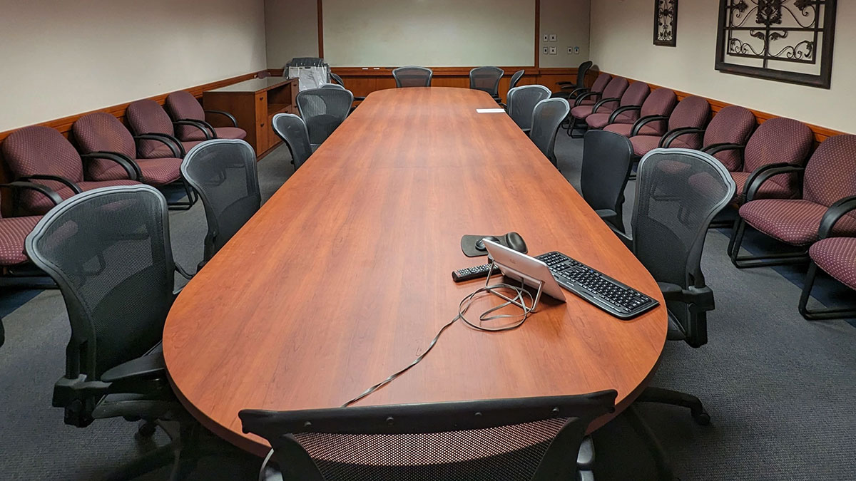 Alternate view of a Pharmacy Hall South conference room with a long oval meeting table, rolling chairs, and additional seating lining the walls.