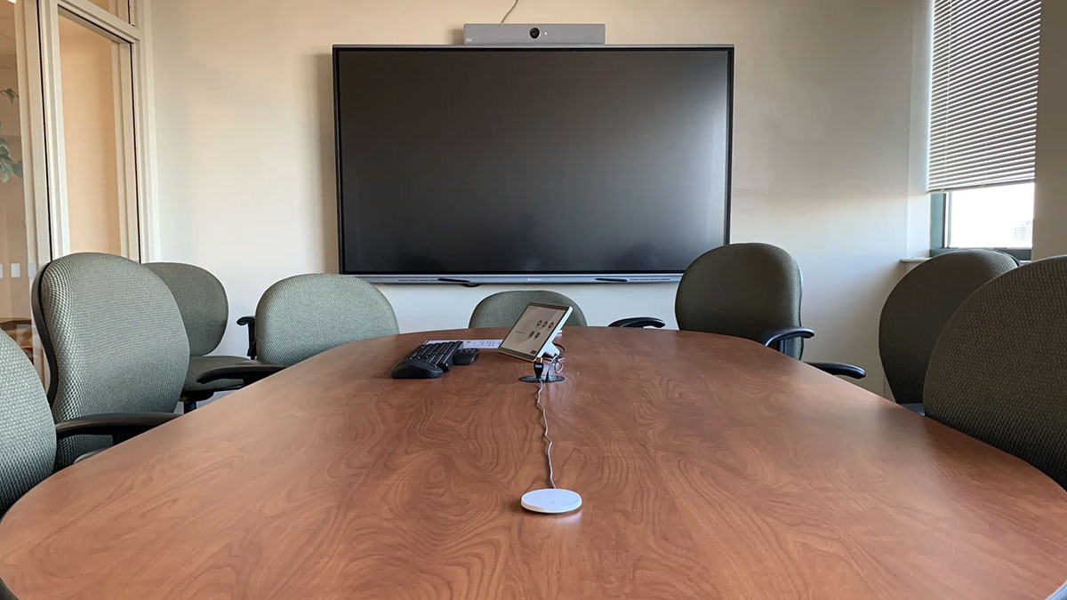 Conference room Saratoga 01‑621 with an oval meeting table, rolling chairs, a wall‑mounted display screen, and integrated video‑conference equipment.