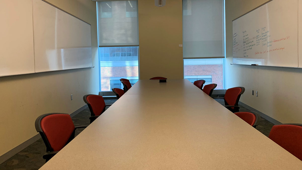 Pharmacy Hall North seminar room with a long conference table, chairs on both sides, whiteboards on opposite walls, and windows at the far end.