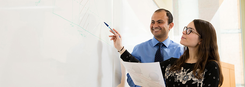 A professor and student work on a white board.