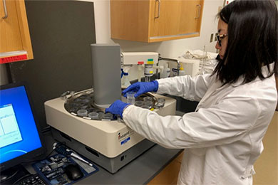 Student in lab coat takes substance out of formulation machine in the Applied Pharmaceutics Lab.