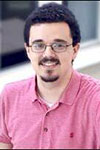 Portrait of Brian Rodenhausen in a pink polo shirt and glasses, against a blurred background.